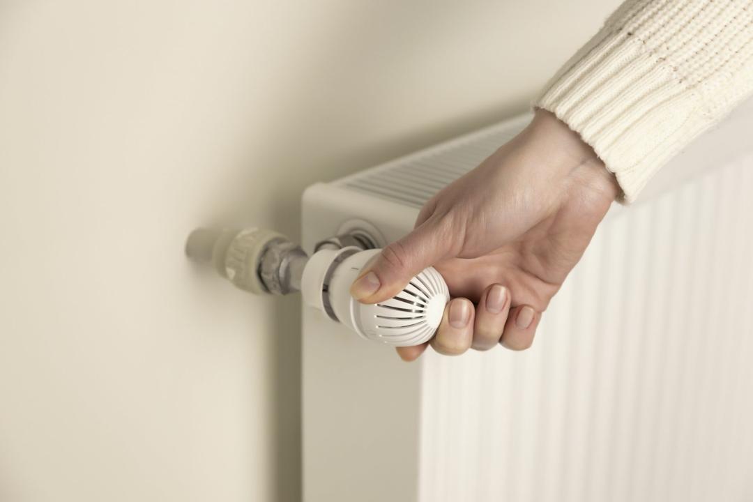A hand turning the thermostatic valve on a white radiator