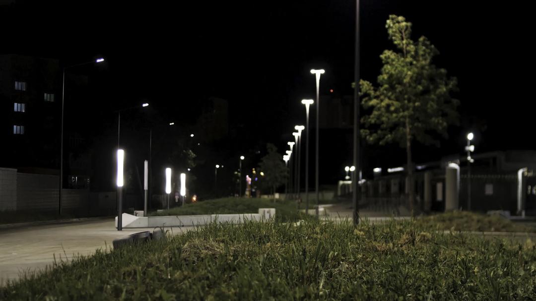 A paved park path lit by tall street lamps at night, with grass in the foreground