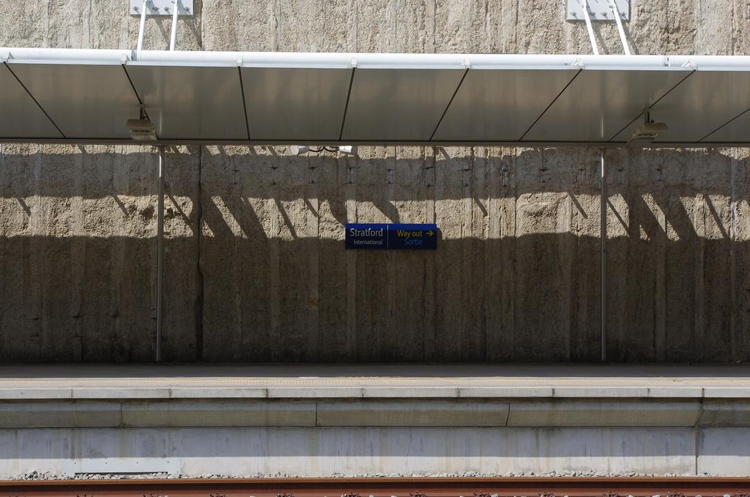An empty platform at Stratford International under a white canopy, with a sign reading "Way out, Sortie" on the concrete wall