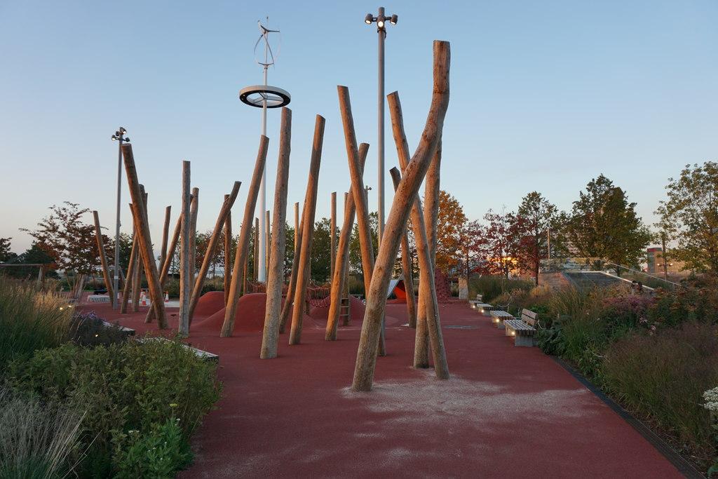 The South Park play area at dusk, with tall timber poles, red climbing mounds and a rope net on a red rubber surface
